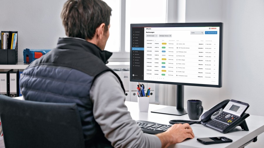 Installateur sitzt an Schreibtisch und schaut auf Computer Bildschirm Installateur sitzt an Schreibtisch und schaut auf Computer Bildschirm