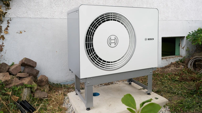 Wärmepumpe steht auf Halterung vor Haus