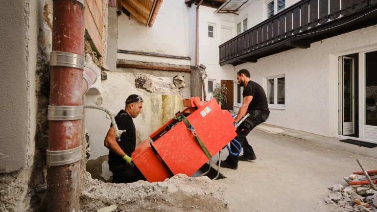 Zwei Männer schleppen eine orangene Ölheizung.
