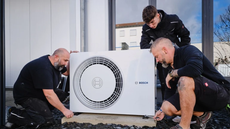 Drei Männer montieren eine Wärmepumpe auf einem Fundament.