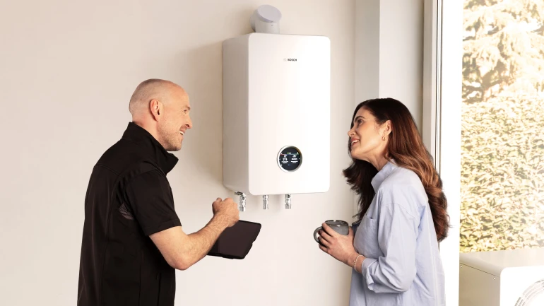 Ein Installateur und eine Frau stehen vor einem wandhängenden Gasbrennwertgerät und unterhalten sich.