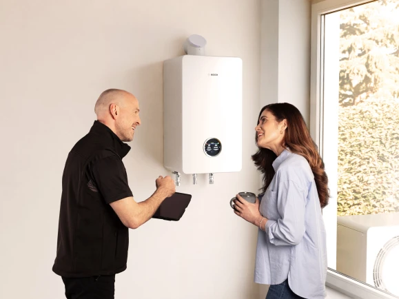 Ein Installateur und eine Frau stehen vor einem wandhängenden Gasbrennwertgerät und unterhalten sich.