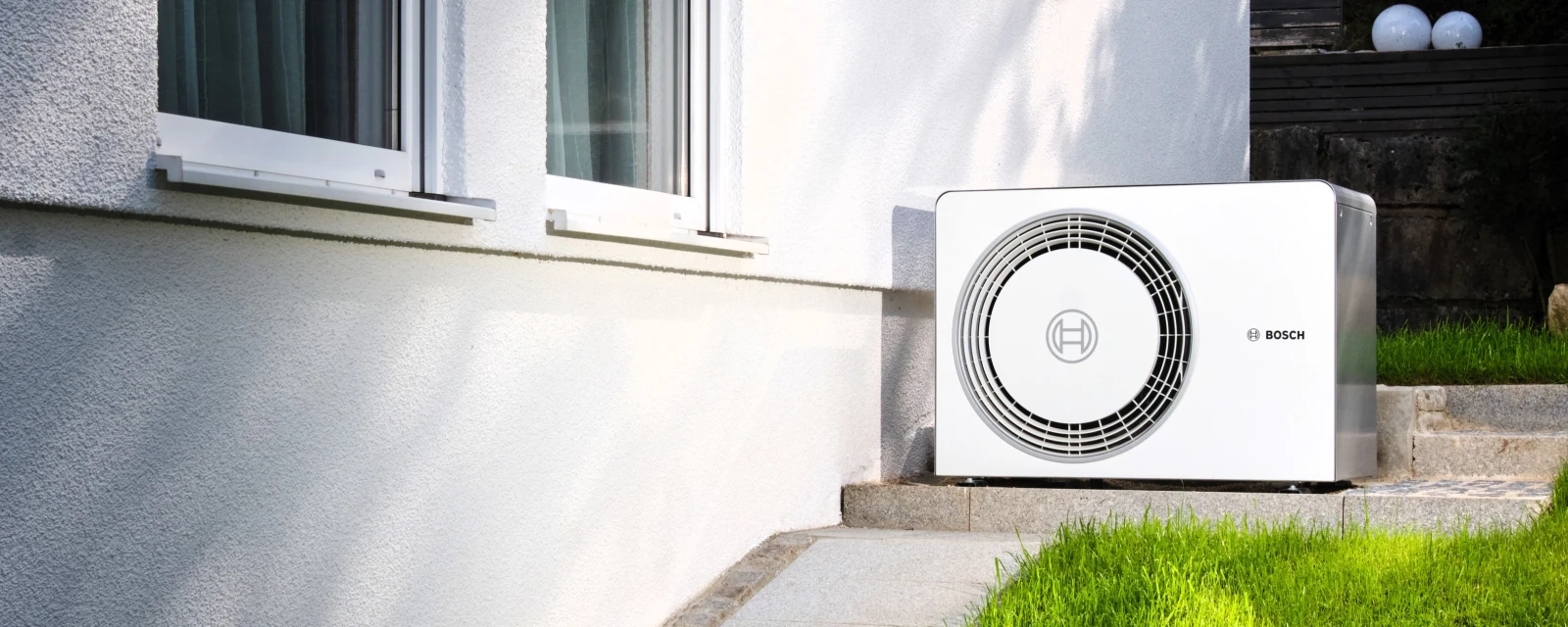 Bosch Wärmepumpe Compress 6800i AW steht an der Hauswand eines weiß gestrichenen Hauses.