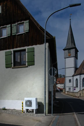 Altes Bauernhaus mit Kirchturm im Hintergrund.