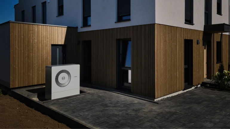 Ein modernes Gebäude mit Wärmepumpe davorstehen.