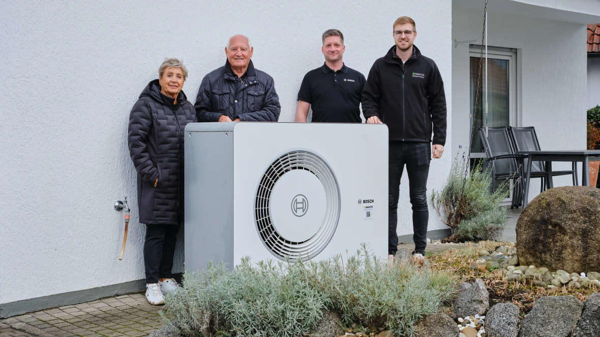 Hauseigentümer und Bosch Installateure stehen hinter der montierten Wärmepumpe am Haus.