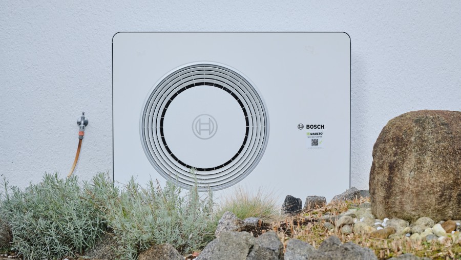 Bosch Wärmepumpe Compress 6800i AW steht an weißer Hauswand. Bosch Wärmepumpe Compress 6800i AW steht an weißer Hauswand.
