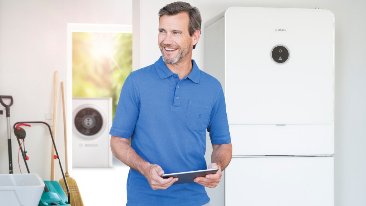 Bosch Luft-Wasser Wärmepumpe 7000i in Garage, daneben steht ein Mann mit einem Tablet Bosch Luft-Wasser Wärmepumpe 7000i in Garage, daneben steht ein Mann mit einem Tablet