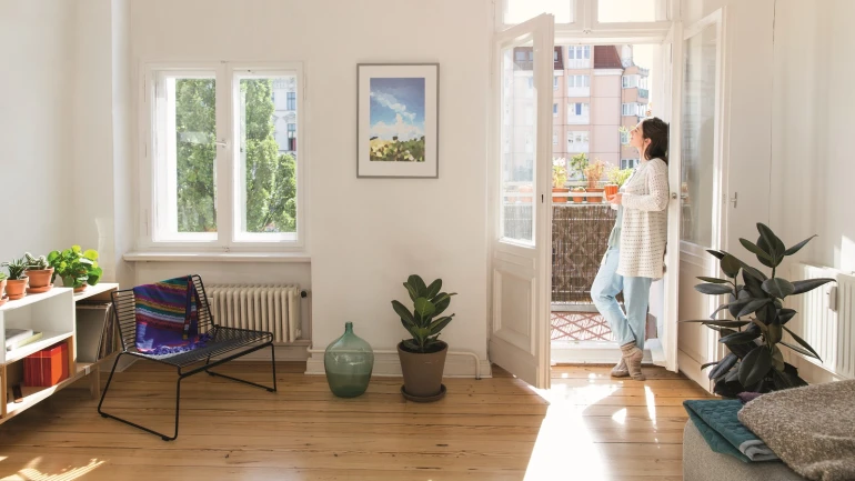 Frau lüftet Wohnung kurz und intensiv und lehnt sich dabei an die offene Balkontür