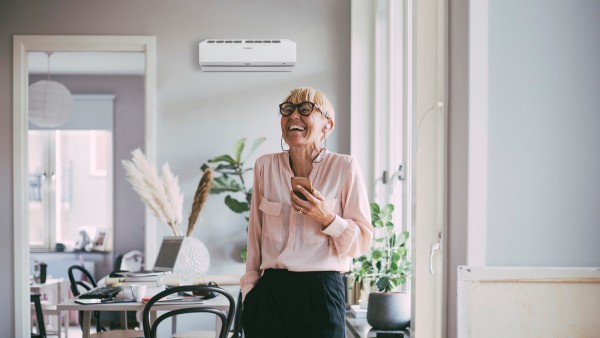 Frau lehnt an Tisch und lacht, im Hintergrund ist eine Klimaanlage zu sehen