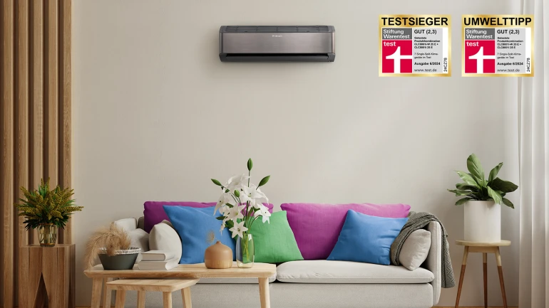 Ein beiges Sofa steht in einem Raum mit vielen bunten Kissen und darüber hängt eine Klimaanlage an der Wand. Rechts danaben sind Textsieger Logos zu sehen.