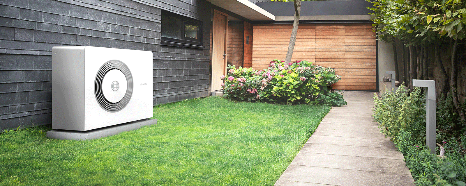 Bosch Wärmepumpe Compress 5800i AW Außeneinheit steht vor einem Haus auf einem Fundament im Garten. Bosch Wärmepumpe Compress 5800i AW Außeneinheit steht vor einem Haus auf einem Fundament im Garten.