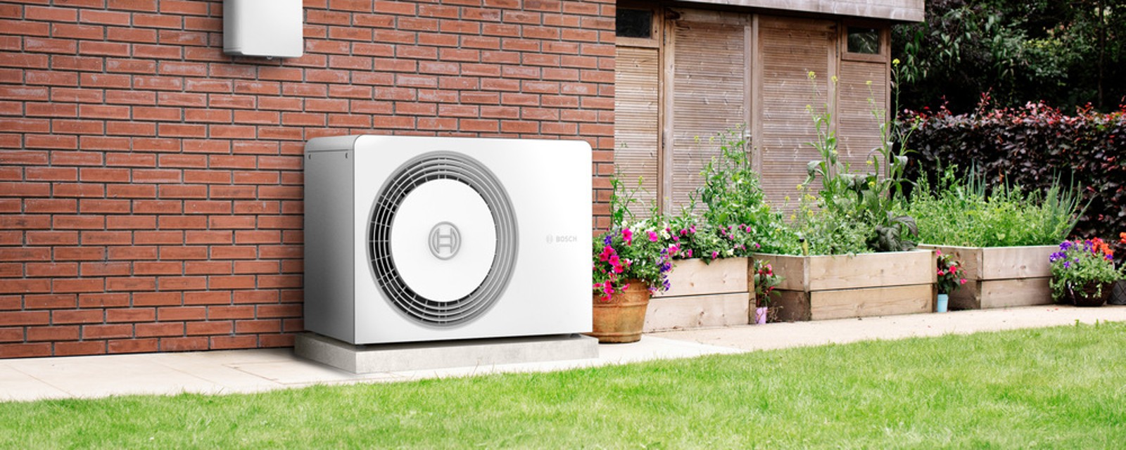 Eine Wärmepumpe von Bosch steht an einer Hauswand im Garten. Eine Wärmepumpe von Bosch steht an einer Hauswand im Garten.