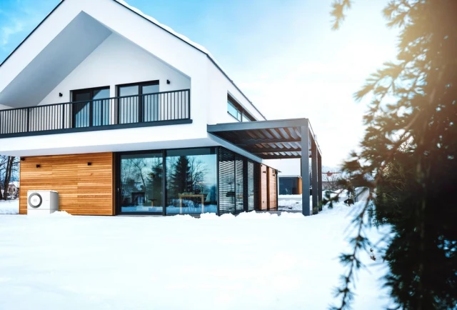 Ein Einfamilienhaus von Schnee umgeben, davor steht eine Bosch Luft-Wasser-Wärmepumpe Compress 5800