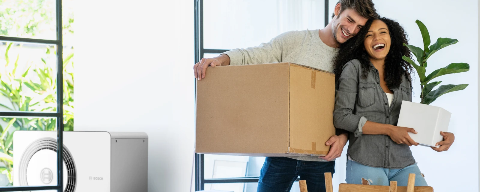 Ein Paar befindet sich im Umzug während auf der Terrasse eine Luft-Wasser-Wärmepumpe zu sehen ist.