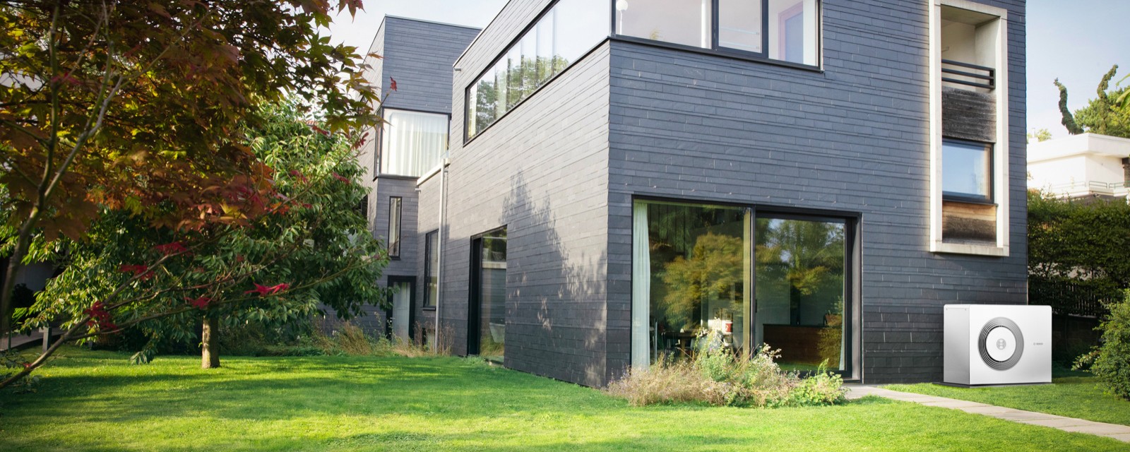 Ein Neubaugebäude mit Garten und Wärmepumpe vor der Hauswand