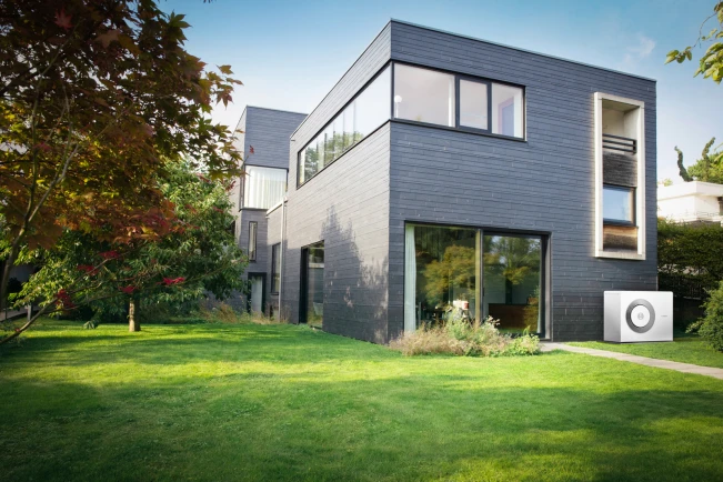 Eine Bosch Wärmepumpe Compress 5800i AW steht an Hauswand eines Einfamilienhauses mit großem Garten.