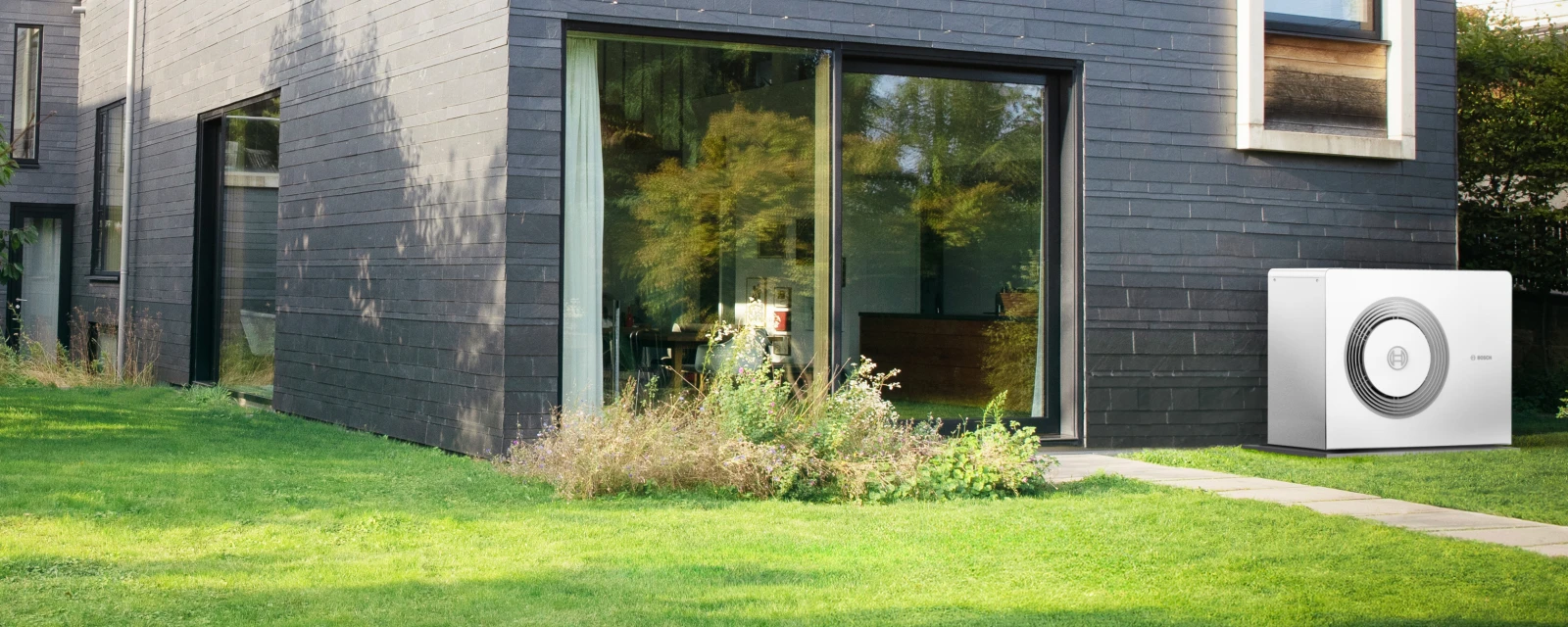 Eine Wärmepumpe Compress 5800i AW steht im Garten an der Hauswand eines modernen Gebäudes.