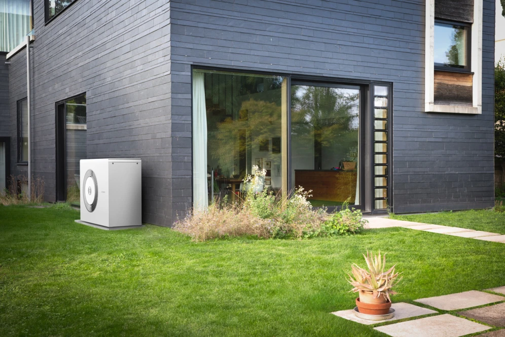 Eine Bosch Wärmepumpe steht im Garten an einer Hauswand.