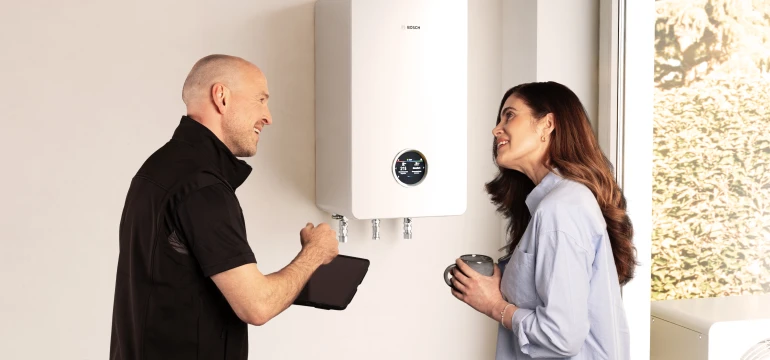 Ein Installateur und eine Frau unterhalten sich über die neue All-in-One Heizung Compress Hybrid 5800i G von Bosch an der Wand