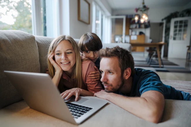 Familie liegt mit Laptop auf dem Sofa.