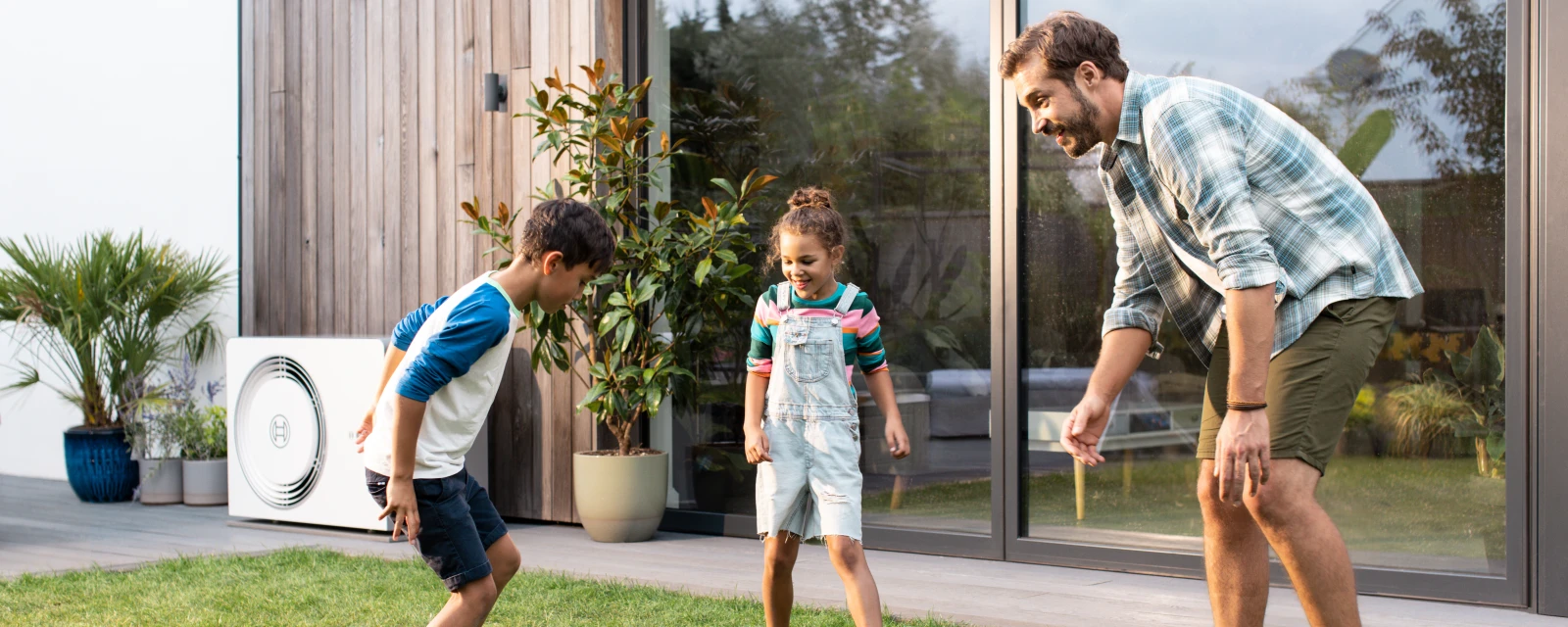 Mann und zwei Kinder spielen im Garten Fußball, im Hintergrund ist eine Wärmepumpe von Bosch an der Hauswand zu sehen.