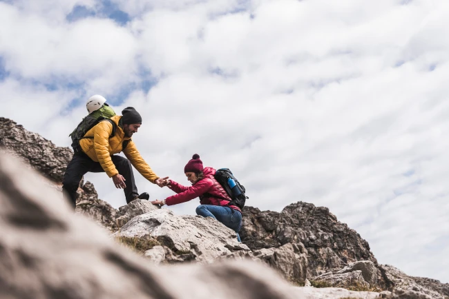 Ein Mann unterstützt eine Frau beim Bergsteigen.