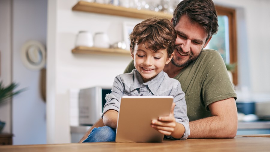 Ein Mann und Kind sitzen in einer Küche und schauen auf ein Tablet. Ein Mann und Kind sitzen in einer Küche und schauen auf ein Tablet.