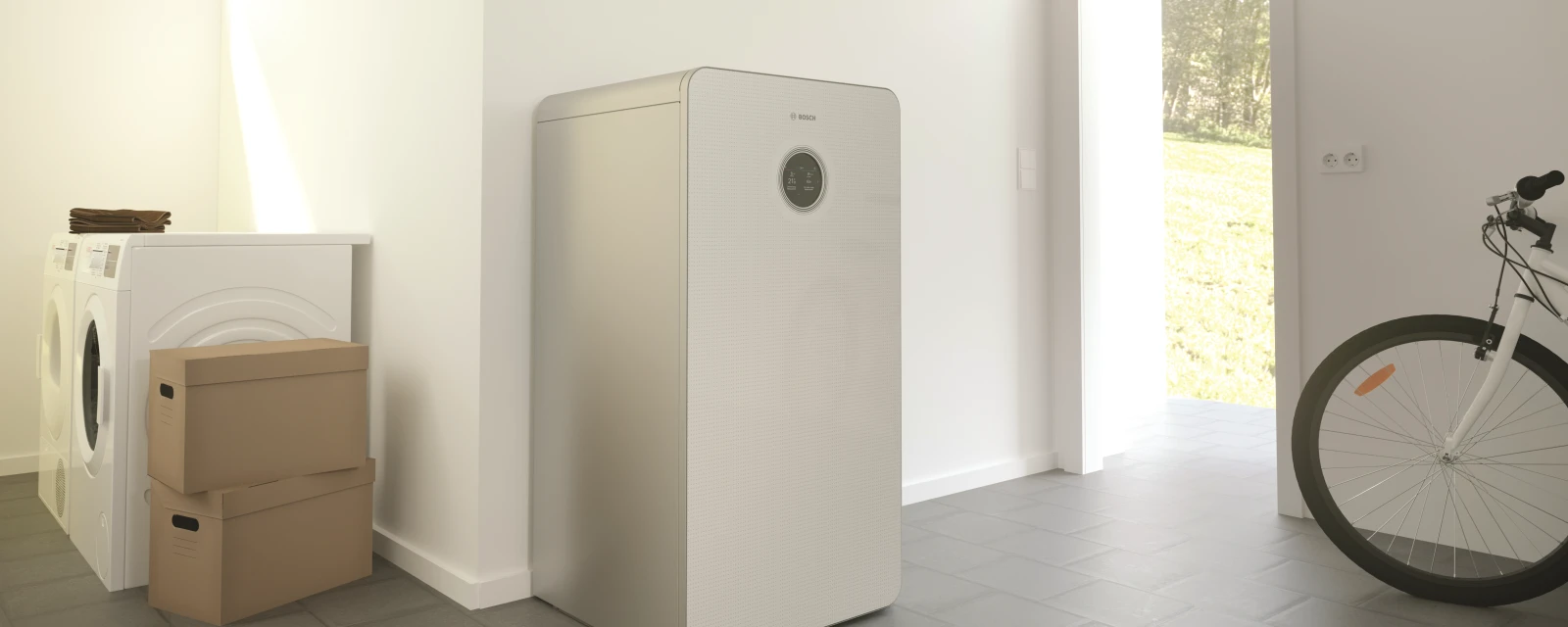 Eine Erdwärmepumpe steht in einem Keller, in dem auch Waschmaschine, Trockner, Kartons und ein Fahrrad stehen.