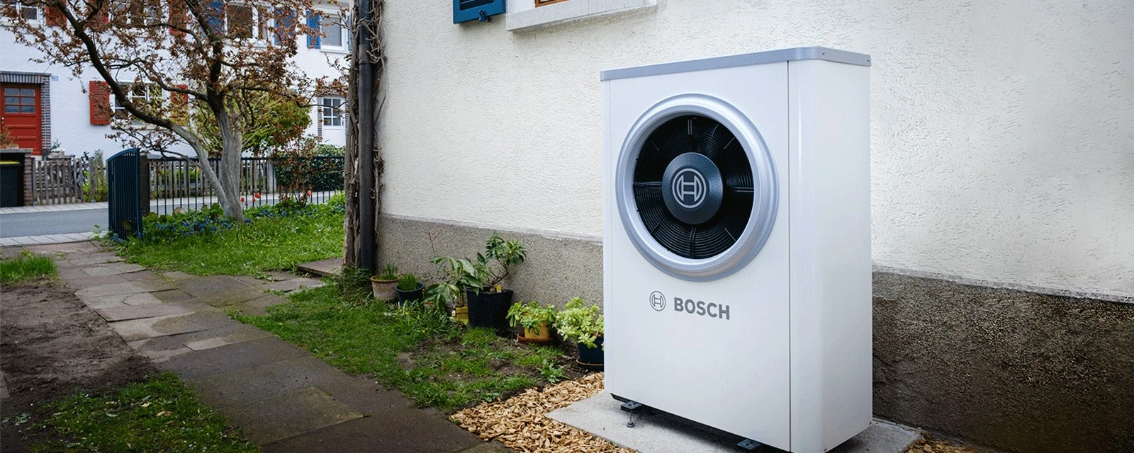 Eine Bosch Wärmepumpe steht vor einem Altbau Haus an der Außenfassade.