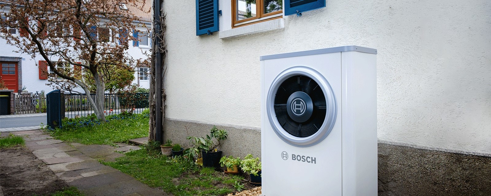 Eine Wärmepumpe steht vor einem Altbau Haus an der Außenfassade.