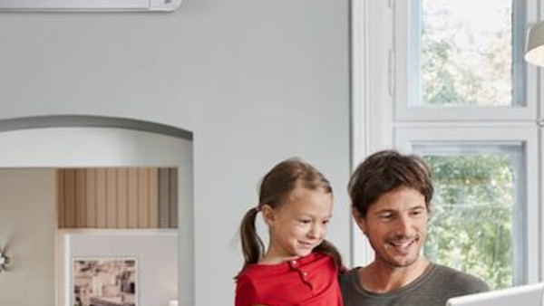 Vater mit Kind auf Arm steht in der Küche und schaut auf Tablet