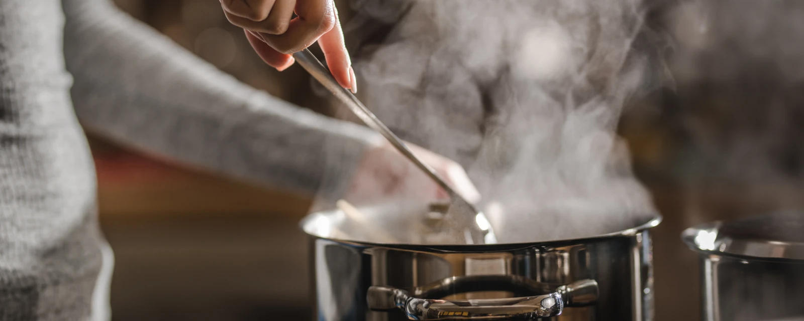 Eine Person rührt in einem Topf aus dem Dampf aufsteigt.