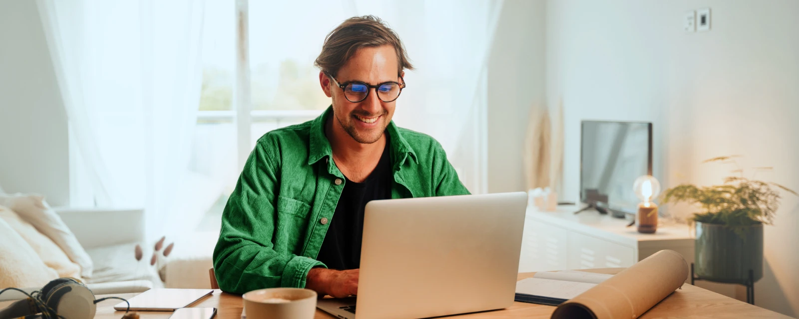 Ein junger Mann sitzt an einem Tisch und schaut auf seinen Laptop.