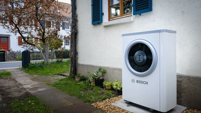 Eine neue Wärmepumpe von Bosch steht an der Hauswand eines Altbaus.