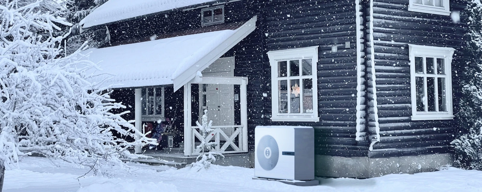 Eine Bosch Wärmepumpen Außeneinheit Compress 8800 steht im Winter vor einem Haus im Schnee