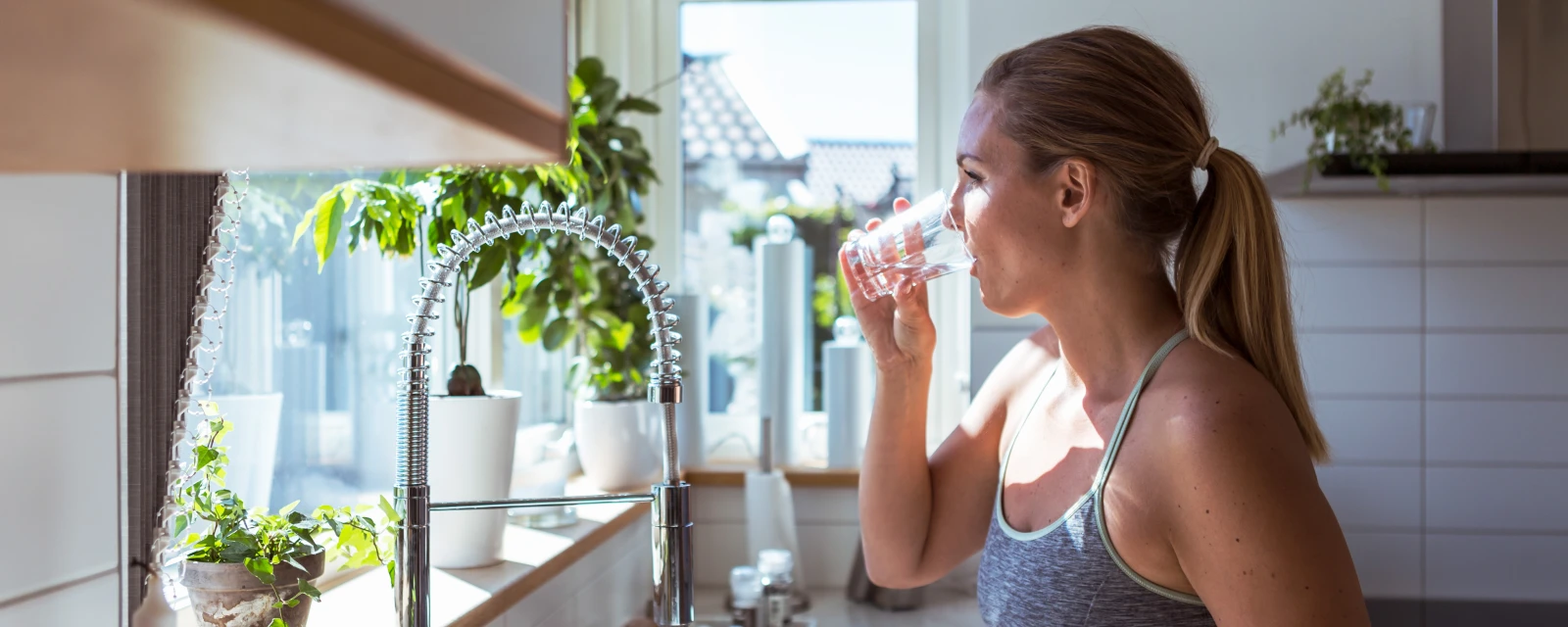 Frau drinkt Leitungswasser aus dem Wasserhahn in der Küche