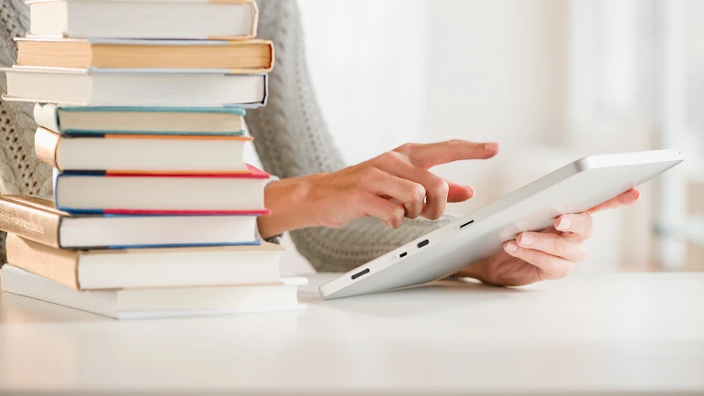 Eine Frau bedient ein Tablet, daneben steht ein Bücherstapel.