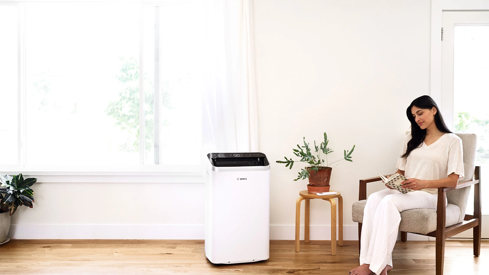 Das mobile Klimagerät Cool 5000 von Bosch in einem Wohnzimmer stehend, daneben eine Frau auf einem Sessel, welche gerade etwas liest.