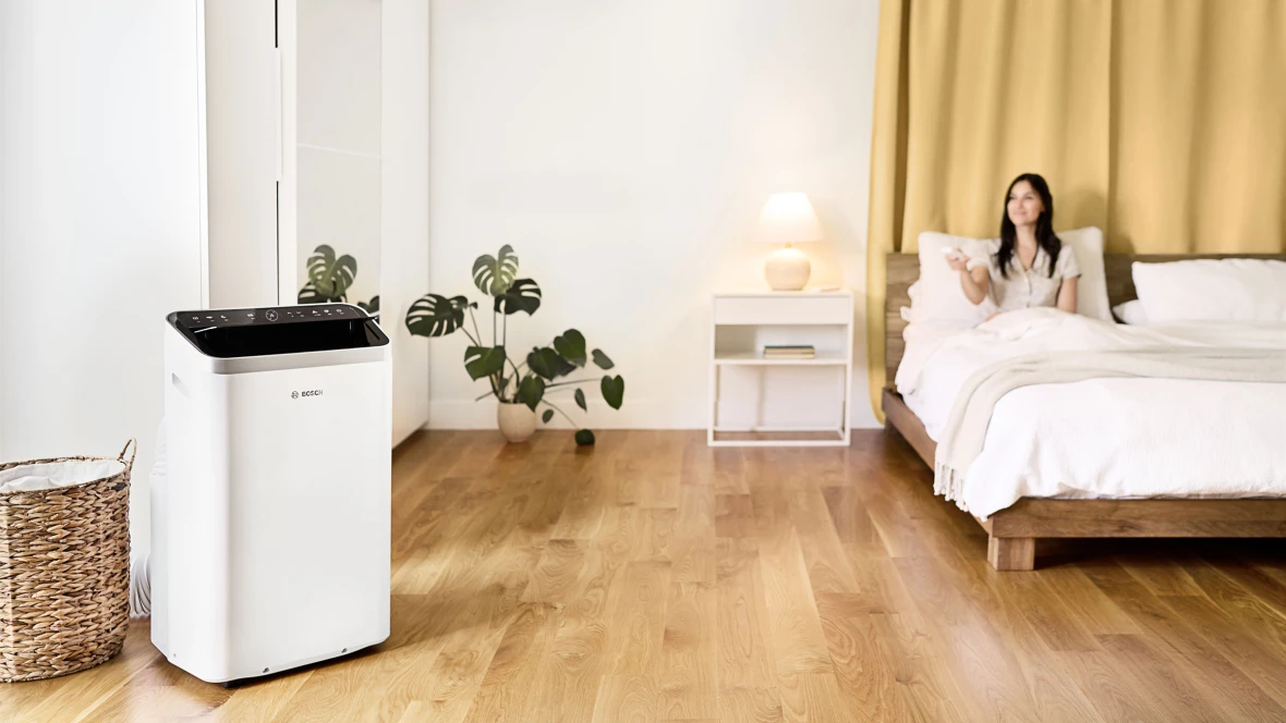 Eine Frau steuert das mobile Klimagerät Cool 5000 von Bosch bequem von ihrem Bett aus.