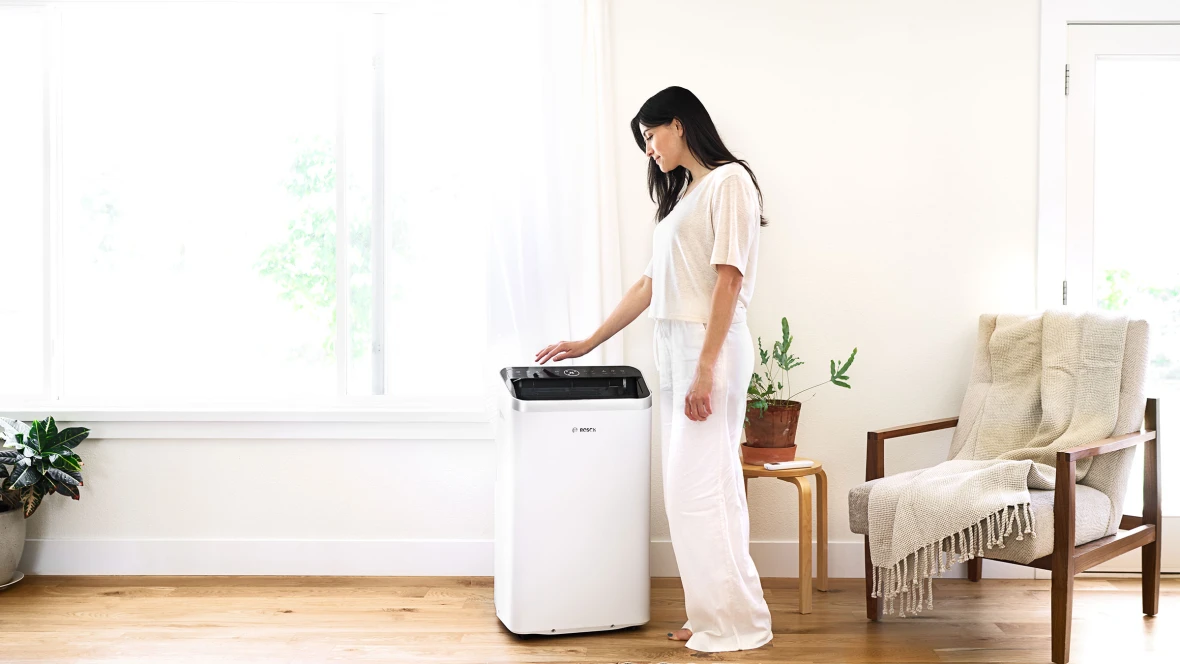 Eine Frau steht in ihrem Wohnzimmer neben dem Klimagerät Cool 5000 von Bosch.