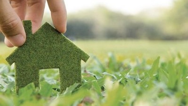Kleines grünes Haus wird von einer Hand auf die grüne Wiese gestellt