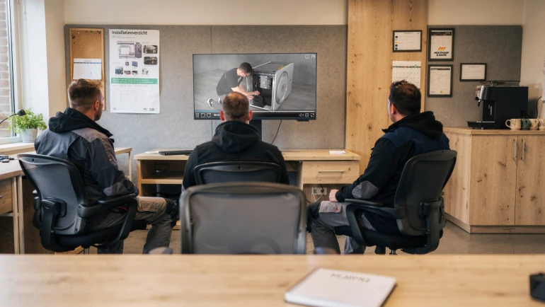 Et team af teknikere deltager i et online videokursus på et moderne kontor. (AI-genereret)