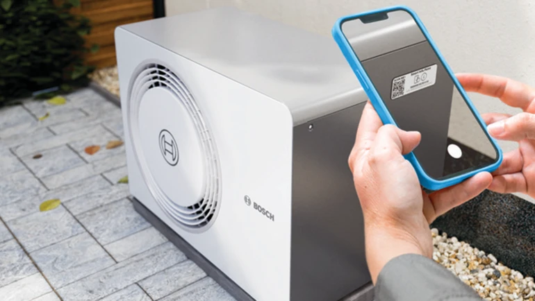 En tekniker scanner en QR-kode på en Bosch udendørs varmepumpeenhed med en smartphone for at få adgang til produktinformation eller til registrering.