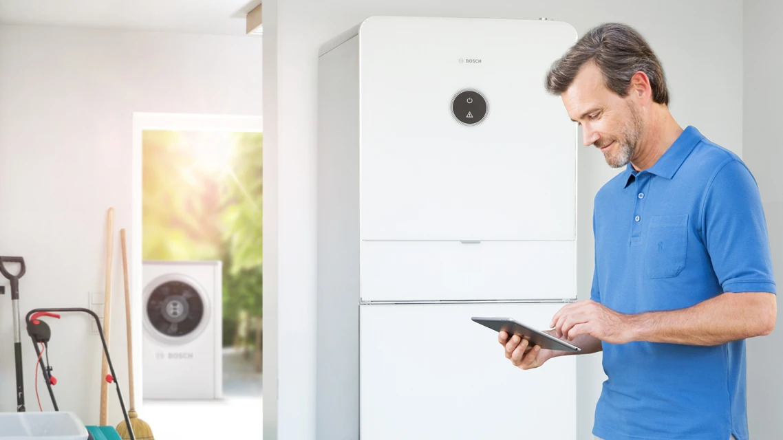 Man standing with tablet in front of the indoor unit of his split heat pump.