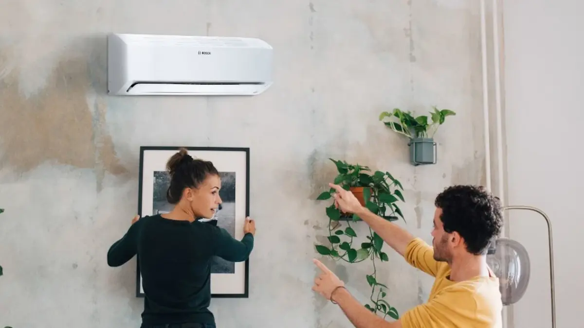 A young couple hanging a picture onto the wall with a Bosch AC above.
