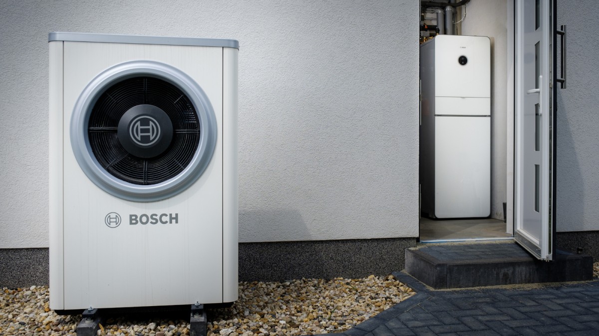 A modern heat pump from Bosch with a high COP stands in front of a house.