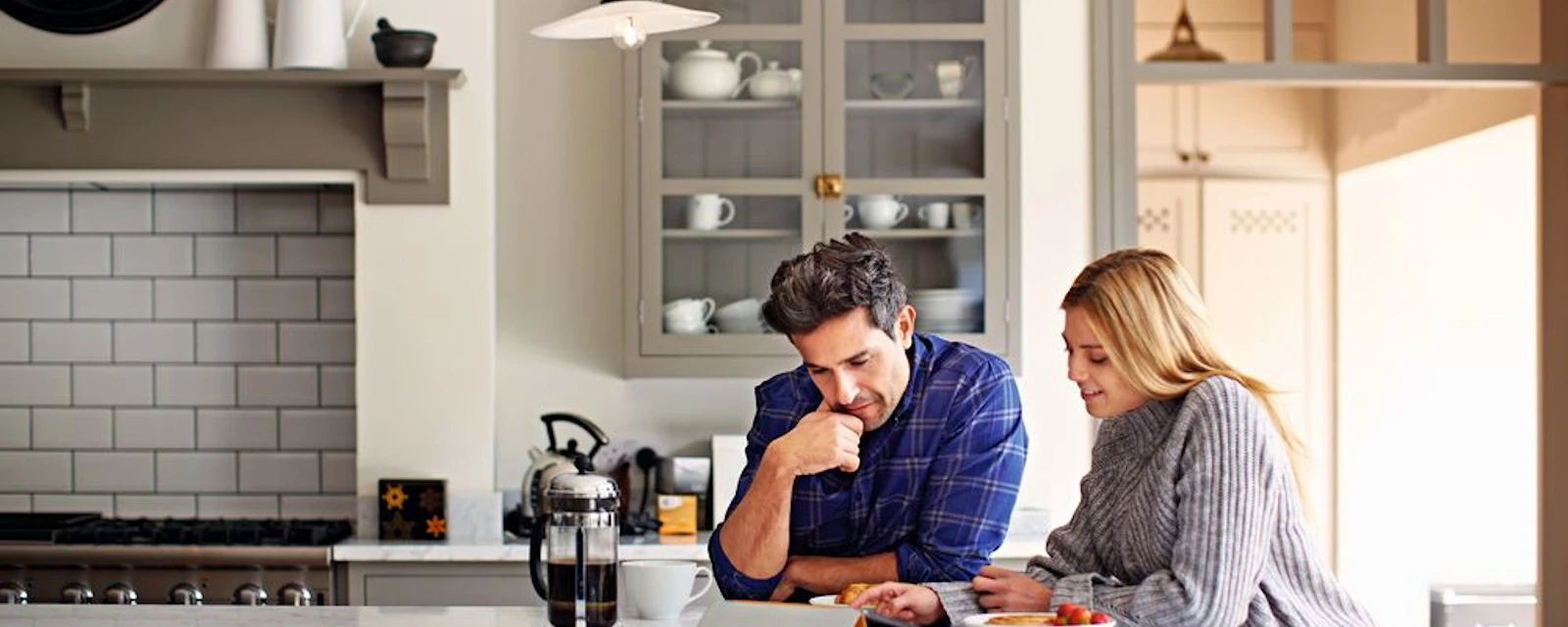 Un jeune couple assis à la table de la cuisine discute des avantages et des inconvénients de la pompe à chaleur ou du chauffage au gaz.