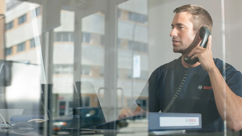 Un employé du service client Bosch est au téléphone et regarde un écran d'ordinateur,