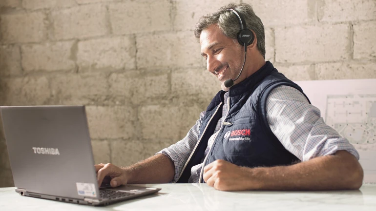 Un technicien du service après-vente de Bosch regarde son ordinateur portable et discute au téléphone avec un client.